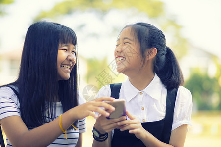 手持智能机与牙齿笑脸相提并论的亚裔青少年快乐面容美丽移动电话伙伴图片