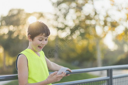 细胞现代的在一个篮球场上看着他的智能手机时笑着微的青少年肖像户外图片