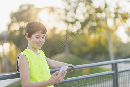 互联网沟通在一个篮球场上看着他的智能手机时笑着微的青少年肖像英俊的图片
