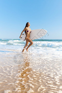 泳衣冲浪女孩带着板向海滩跑去图片