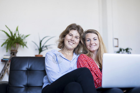 浏览学生们两个微笑的年轻女人坐在沙发上用笔记本电脑请享用图片