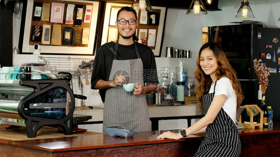 快乐的男年轻亚洲小企业所有者快乐亚洲男子女律师协会服务员在咖啡店厅柜台的字体中微笑女服务员创办新的食品和饮料业中的男女伙伴关系商图片