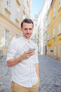 维也纳街上带智能手机的年轻人带着城市和背包的男游客在欧洲街上的白种男孩看欧洲城市寻找欧洲城市微笑地标图片
