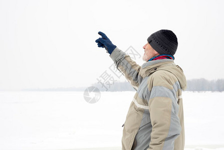 一个戴羊毛帽防水夹克和羊毛帽的男人在雪下寒冷而悲伤的冬季清晨用手指靠近第尼珀尔河指着一些东西成熟一种图片