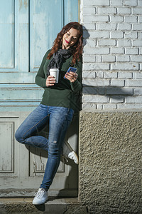 饮料城市的户外有红发年轻姑娘看着她的手机喝茶杯里的咖啡喝着外卖图片