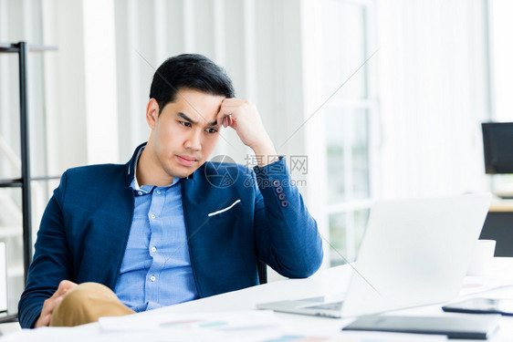 坏的公司坐着精神紧张商人从事笔记本电脑工作在商业损失后头痛在办公室背景中图片