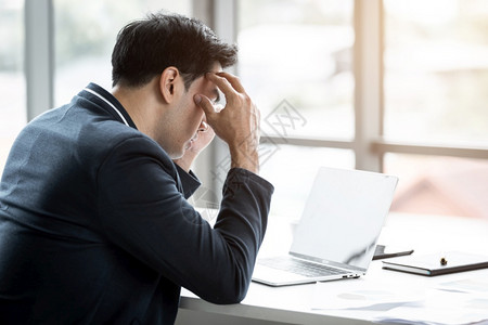 精神紧张的商人从事笔记本电脑工作在商业损失后头痛在办公室背景中员工担心失败背景图片