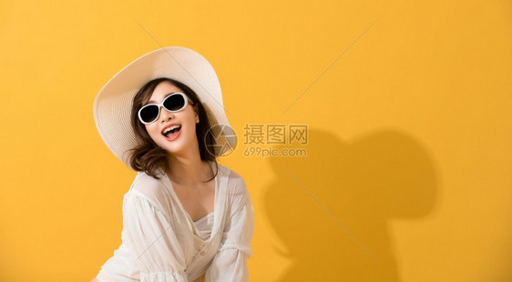 亚洲美丽的快乐年轻女夏天带着太阳眼镜和帽子笑着欢的夏天看着黄色工作室背景上隔绝的摄影机亚洲人们吸引的图片