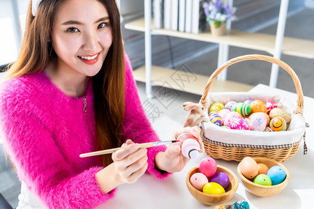 家年轻的复活节概念带着兔子耳朵的亚洲快乐年轻女披着兔子耳朵的青春少女为复活节画了鸡蛋在白衣室背景下象征图片