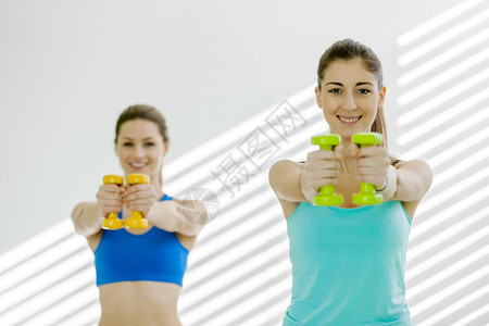 快乐的运动员力量两名有吸引的年轻女子在健身房做哑铃运动的照片图片