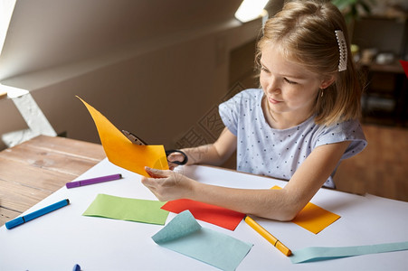 丰富多彩的玩小姑娘在桌子上剪彩纸小孩在桌边剪彩纸艺术学校的创意课上年轻画家愉快爱好乐童年小女孩剪彩纸子在工作间调色板图片