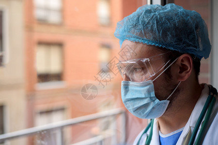 外套戴面罩的医生透过院窗户看戴面罩的医生透过窗户看口罩严肃的图片