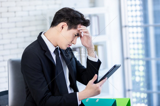 亚洲人经理社会的精神紧张商人用平板片工作在失去商业损后头疼在办公室背景中图片