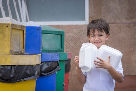 男孩把泡沫塑料盒放在垃圾桶里将泡沫箱装进家里的外卖食品箱中造成污染不能再使用离开化学环境的图片