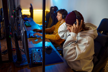 在电子游戏俱乐部虚拟娱电子体育锦标赛网络运动生活方式中玩耳机的两名青年游戏家在电子俱乐部里玩双名青年游戏家少专业的展示图片