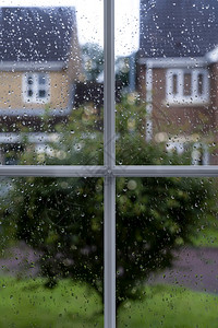闪耀在雨天窗玻璃上有雨滴树和房子背景模糊在路面下着雨后用水滴纹理看望窗边的透过框风景细节图片
