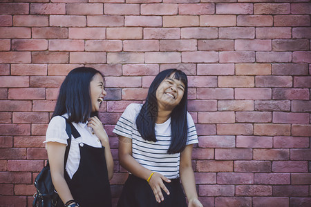 刘海两个亚裔青少年笑着带快乐的情绪站在红砖墙边立年级乐趣图片