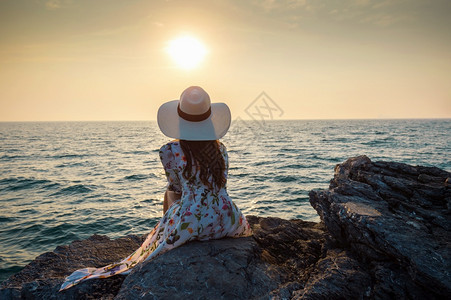 坐在岩石顶端的年轻女人看着海边和西昌岛的日落丰富多彩的常设图片