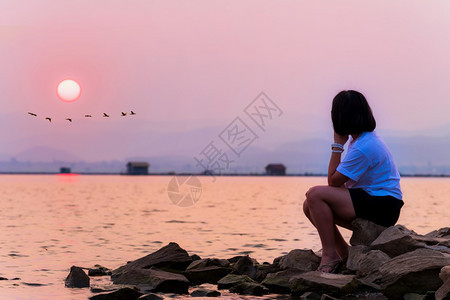 素攀旅行排亚洲少女独自孤单地坐在水边看着美丽的自然景观太阳和鸟群在湖底KrasiaoDam泰国SuphanBuri泰国Krasi图片