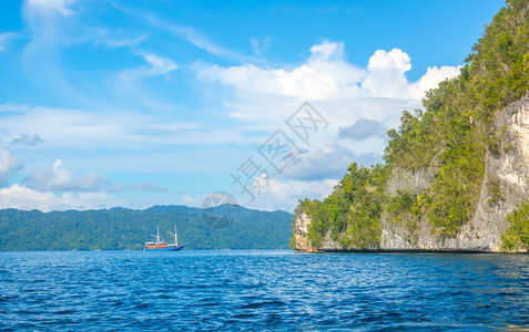 海滩旅行印度尼西亚热带岛屿的岩石海岸阳光明媚的天气中印度尼西亚热带岛屿的沿海岩礁与雨林和远洋游艇相距遥的山坡游艇上雨林结石图片