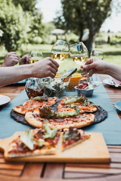 喝一种人们朋友在夏季野餐室外晚宴期间在一家庭花园里做吐司朋友在一家庭花园里做吐司在夏日野餐室外晚宴中朋友在后院果园里的一个用披萨图片