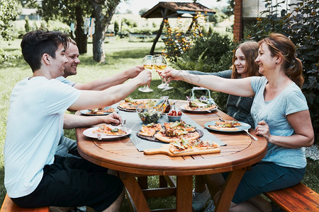 朋友在夏季野餐室外晚宴期间在一家庭花园里做吐司朋友在一家庭花园里做吐司在夏日野餐室外晚宴中朋友在后院果园里的一个用披萨沙拉和水果图片
