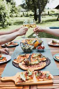 葡萄酒粘合朋友在夏季野餐室外晚宴期间在一家庭花园里做吐司朋友在一家庭花园里做吐司在夏日野餐室外晚宴中朋友在后院果园里的一个用披萨图片