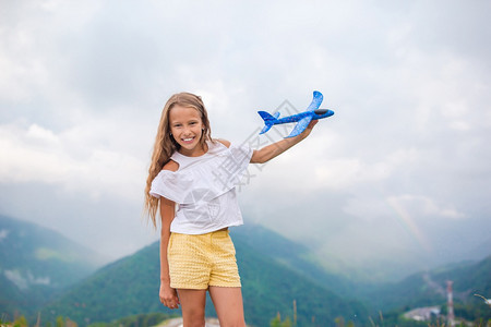 梦山中暑假时漂亮孩子的肖像快乐小女孩玩具飞机在山上手握着玩具机保持蓝色的图片