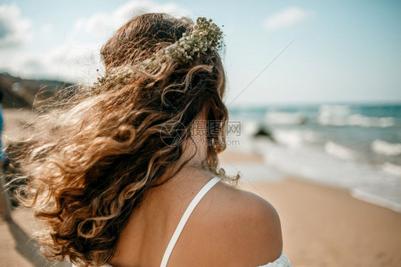 头发在海滩上穿着白色婚纱的新娘头部从背面看到一朵花圈幸福吸引人的图片