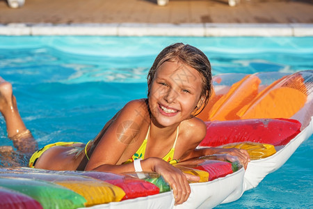 采取小女孩在游泳池里坐充气床垫在游泳池里玩戏和泳池的乐趣小孩在水里玩暑假的概念树干户外图片
