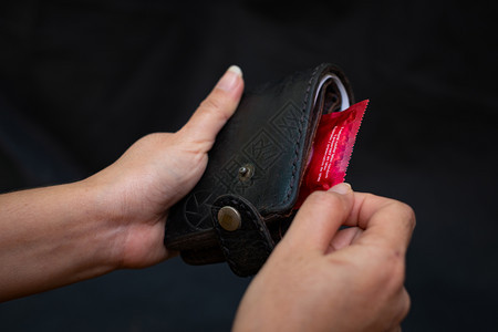 近身妇女手握黑色皮衣钱包底带红色避孕套安全行为和保健以及医疗概念情人节安全与保健风险艾滋图片
