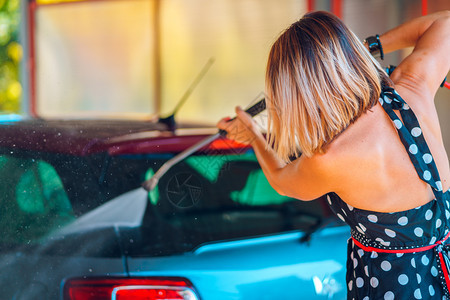 暑期妇女穿着自助洗车服务在加油站使用高压水喷气式机洗车手辆垫圈图片