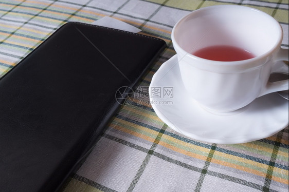 晚餐站在桌上的白茶杯和一个黑色文件夹上面有付款收据一杯茶和个黑色文件夹上面有付款单客人货币图片