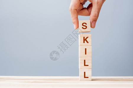 保持目标训练手握木制立方块的商人手SKILL公司在表格背景学习知识研究培训和经验概念上写有SKILL商业词图片