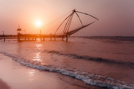 热带海滩的日落洋岸景观与渔网剪影在科钦南印度喀拉邦科钦鱼网地标浮桥图片