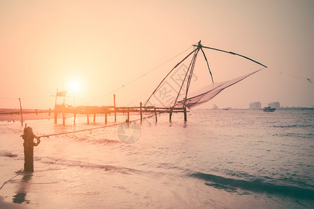 旅行热带海滩的日落洋岸景观与渔网剪影在科钦南印度喀拉邦科钦渔民轮廓图片