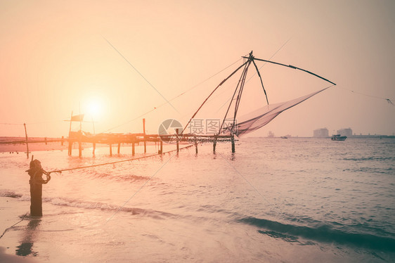 旅行热带海滩的日落洋岸景观与渔网剪影在科钦南印度喀拉邦科钦渔民轮廓图片
