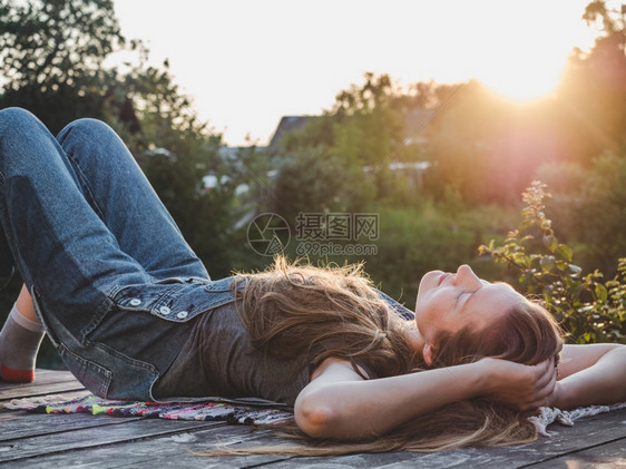 聪明的成人公园美貌女躺在日落背景的木制露台上切合侧视户外休息概念和放松美貌女人躺在木制露台上图片
