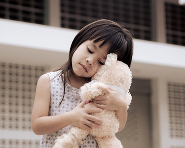 抱着她的泰迪熊可怜小女孩站在家庭后院留中以隔离冠状流行防止这种病畅快停留生活图片