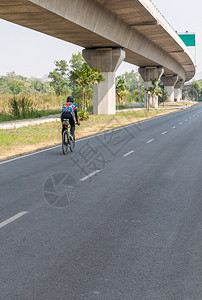 年轻人骑着现代自行车在柏油街上高速公路桥下面的骑自行车活动乐趣图片