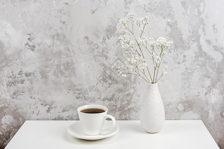房间一杯咖啡和束小花满天星放在白桌上的花瓶里放在灰色的石墙上复制空间最小的风格概念早上好和咖啡时间最小的风格概念早上好和咖啡时间图片