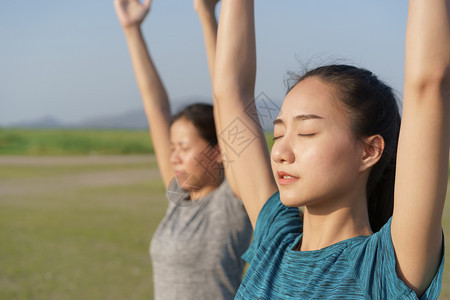 草地尽管做瑜伽的亚洲组人在祈祷姿势和举起手边站在夏天外户时亚洲女孩用冥想方式照顾自己的健康概念和生活方式12月日团体图片