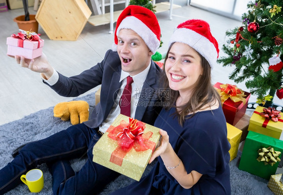 快乐的新年20快乐概念是幸福的情侣在工作完成后拿着礼物交换并在圣诞节和新年树夏夜晚会圣诞背景上赠送礼物一种问候图片