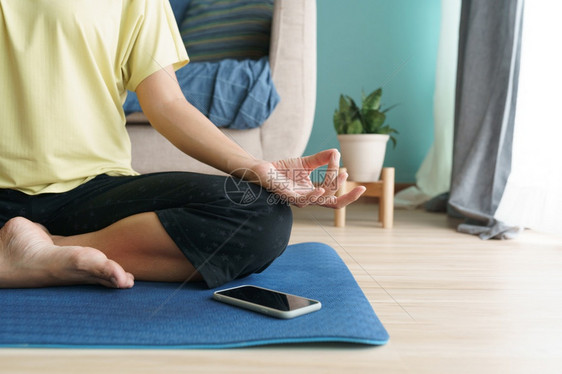 健康地面坐在晚间瑜伽时手露脸的妇女亚洲做瑜伽在家使用移动电话的在线培训员进行家用手机上的放松和冥想概念垫图片
