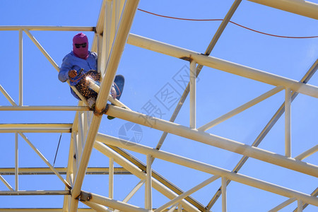 风险电男人亚洲焊接机在建筑工地屋顶结构中以蓝色天空背景为参照的焊接器金属的低角度视图图片