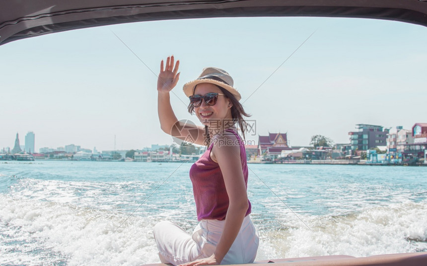 自然日落海身戴帽子和太阳镜的亚洲美丽妇女坐在具有美丽风景背的船上挥手时她戴着帽子和太阳眼镜图片