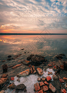 日落时盐湖的全景观仰望着夏日夕阳红光下湖面的石头黎明灾难木制的背景图片