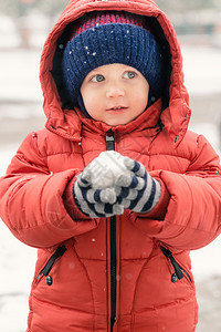 男生为了在下雪时美丽的小男孩看着空虚手里拿雪球上面盖红冬夹克和羊毛帽贴近了脸部喜悦图片