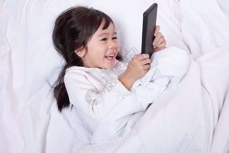 细胞一种家亚洲小孩玩智能手机得开心早上躺在床坐软枕头笑起来感觉很快乐的喜悦图片