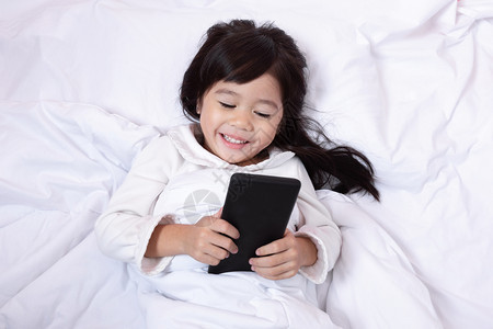 细胞亚洲小孩玩智能手机得开心早上躺在床坐软枕头笑起来感觉很快乐的喜悦青少年孩子图片